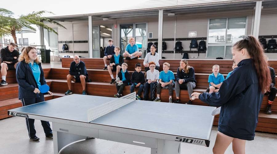 Students enthusiastically cheering on their peers as they compete in a table tennis match.