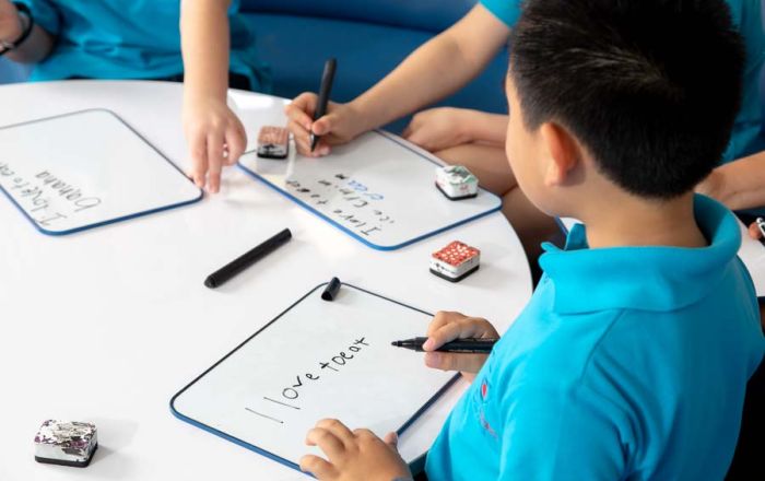 Junior School students practicing writing on small whiteboards in the classroom.